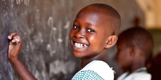 A 9-year-old schoolgirl in Uganda smiles brightly as she practices writing numbers on a chalkboard in her classroom thanks to a charity for children's education. Photo credit: Jordan. J. Hay, 2012.