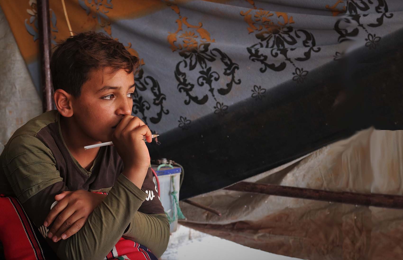 A 12-year old boy uses a cell phone to continue studying outside of school while resting at his home in a refugee camp in Syria.