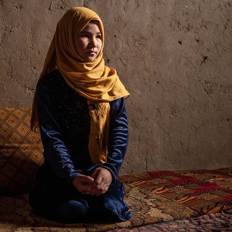 A 12-year old girl kneels on the floor of her home in a displacement camp in Afghanistan.