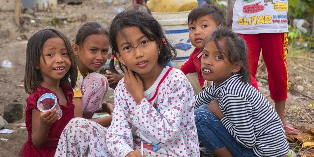 A group of seven young children are gathered in a space littered with branches, blankets and trash. When their homes were destroyed in the 2018 Indonesia earthquake and tsunami, they lived in a temporary shelter and survived on supplies provided by Premiumaid Foundation and other aid organizations. Photo credit: Ardiles Rante / Premiumaid Foundation, Oct 2018.