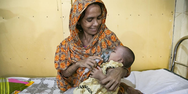 A mother smiles while giving a nebulizer treatment to her baby.