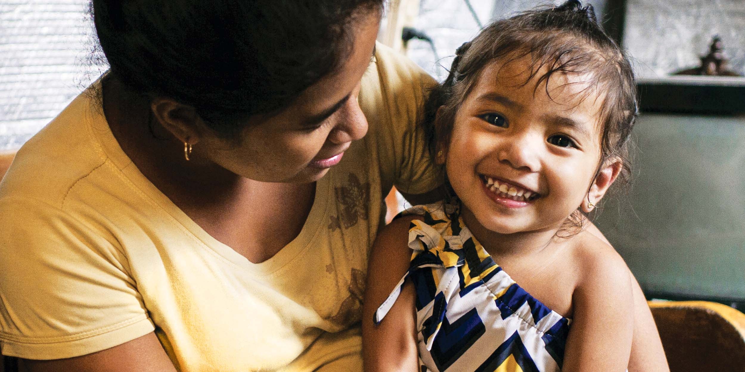 A young girl smiles and sits on her mother's lap.