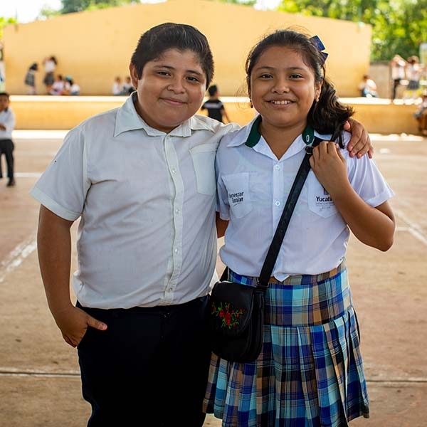Two school children stand next to one another outside a school in Mexico.