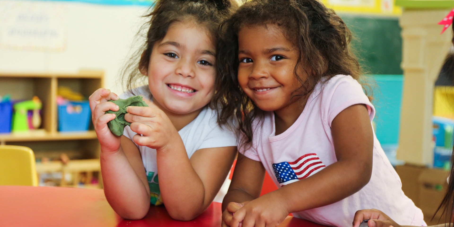 Two young girls stand together smiling at the camera.